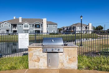 A gas grill in front of a fence with apartments in the background